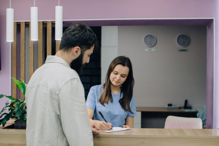 Healthcare professional assisting patient with paperwork at clinic reception area, representing medical administration and client service